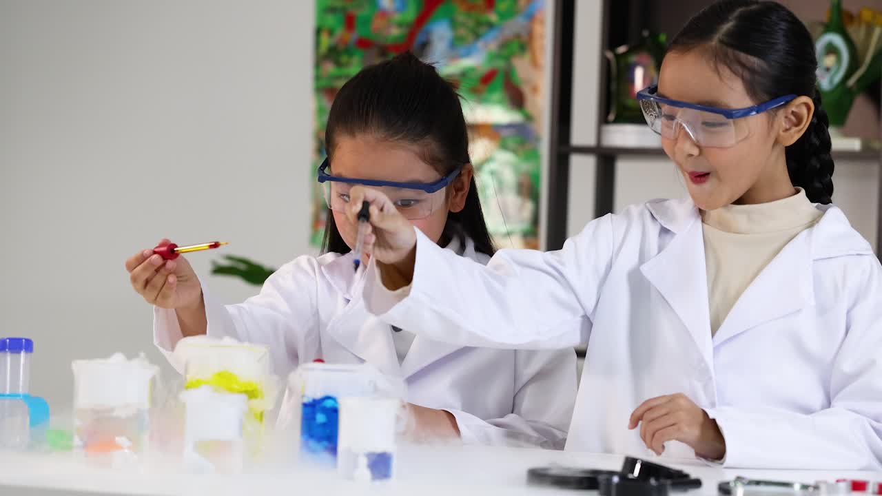 Two girls in lab coats use pipettes for a colorful dry ice experiment in laboratory