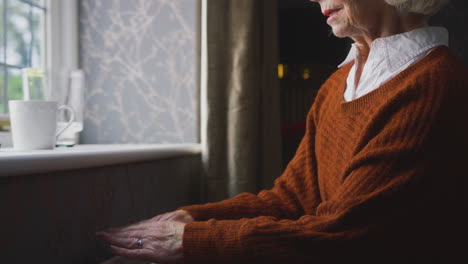 Close-Up-Of-Senior-Woman-With-Hot-Drink-Trying-To-Keep-Warm-By-Radiator-At-Home-In-Energy-Crisis