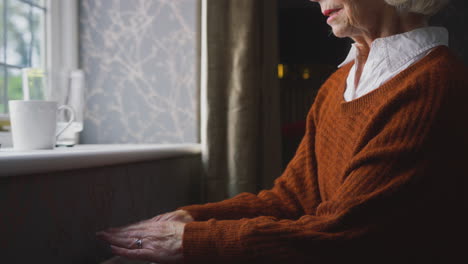 close up of senior woman with hot drink trying to keep warm by radiator at home in energy crisis