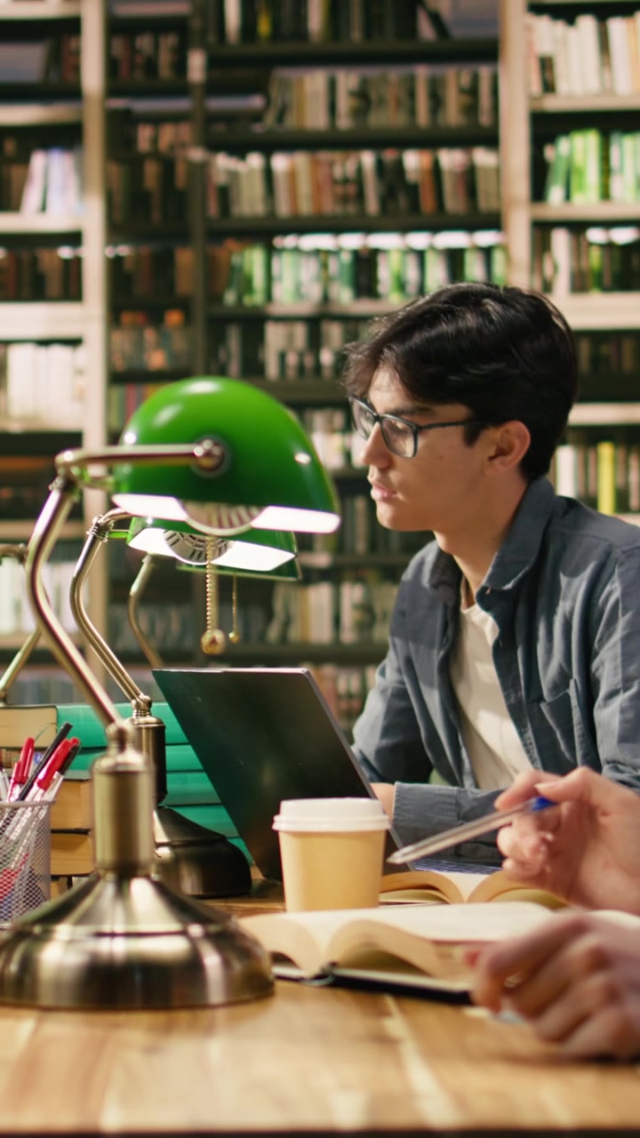 Video verticale. Studenti universitari che discutono con un tutor e studiano con libri aperti.
