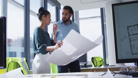 two diverse male and female colleagues holding architectural blueprint and discussing