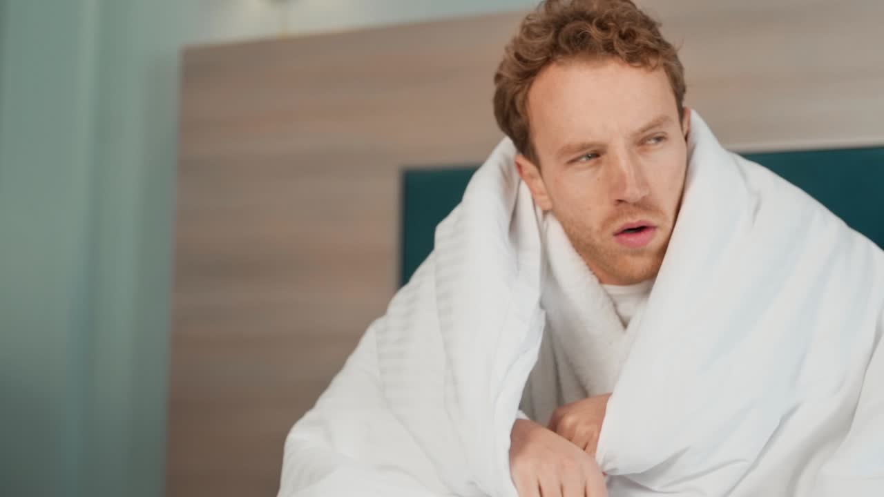 담요로 싸인 못생긴 남자가 침대에서 기침을 한다