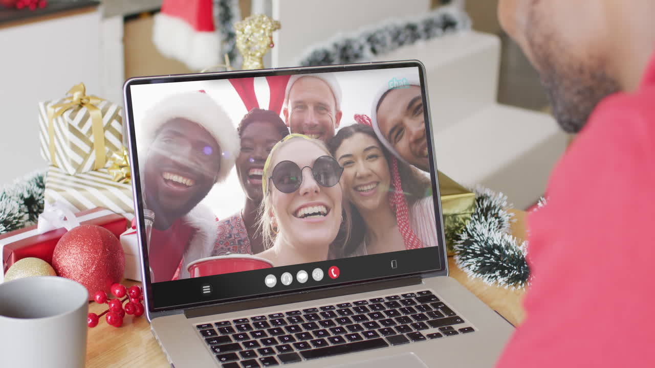 hombre afroamericano con sombrero de santa teniendo llamada de video portátil con amigos diversos felices