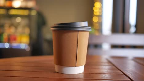 a paper cup of coffee on a wooden table in a cafe