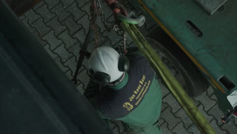 Worker-in-a-helmet-tightening-steel-cables-for-transport-of-large-machinery,-overhead-view