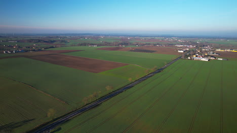 Vista-Aérea-De-La-Carretera-Rural-Polaca-A-Través-De-Campos-Agrícolas-Verdes-Junto-Al-Pueblo-De-Polonia-En-Un-Día-Soleado