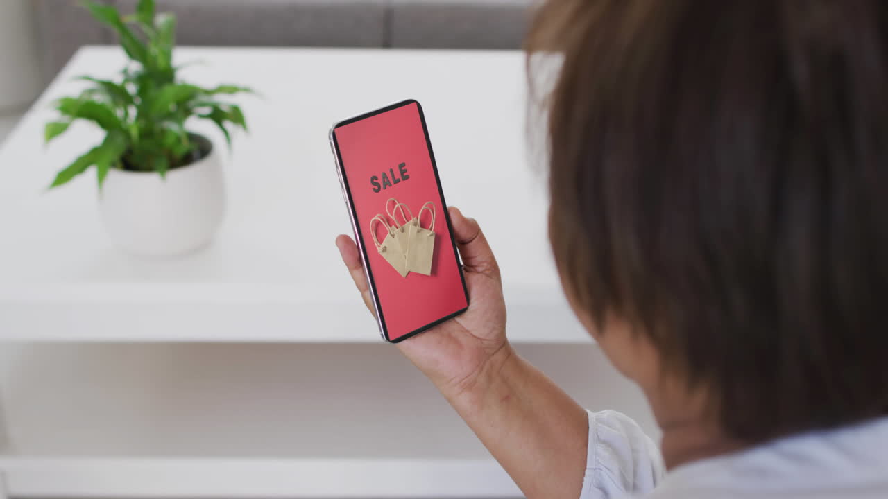 mujer biracial usando teléfono inteligente en casa para comprar en línea, cámara lenta