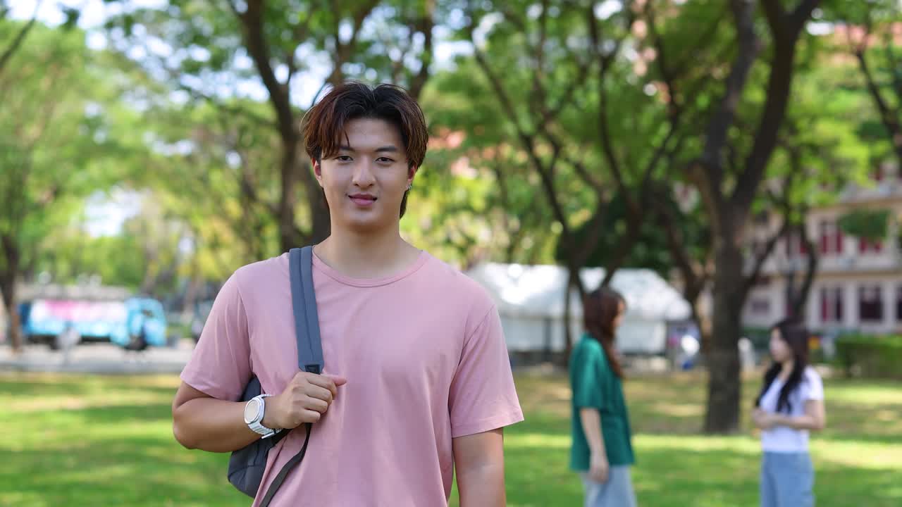 ピンクのシャツを着た若いアジア人男性が、公園でバックパックを背負っています。