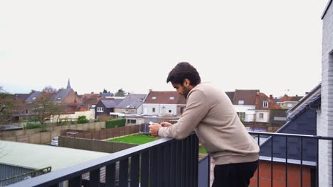 young handsome man standing on his balcony and texting on his phone