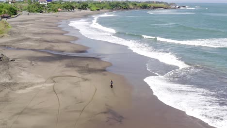 dirt bike rider fun ride on a sandy beach in bali, indonesia with calm waves breaking, top down aerial view