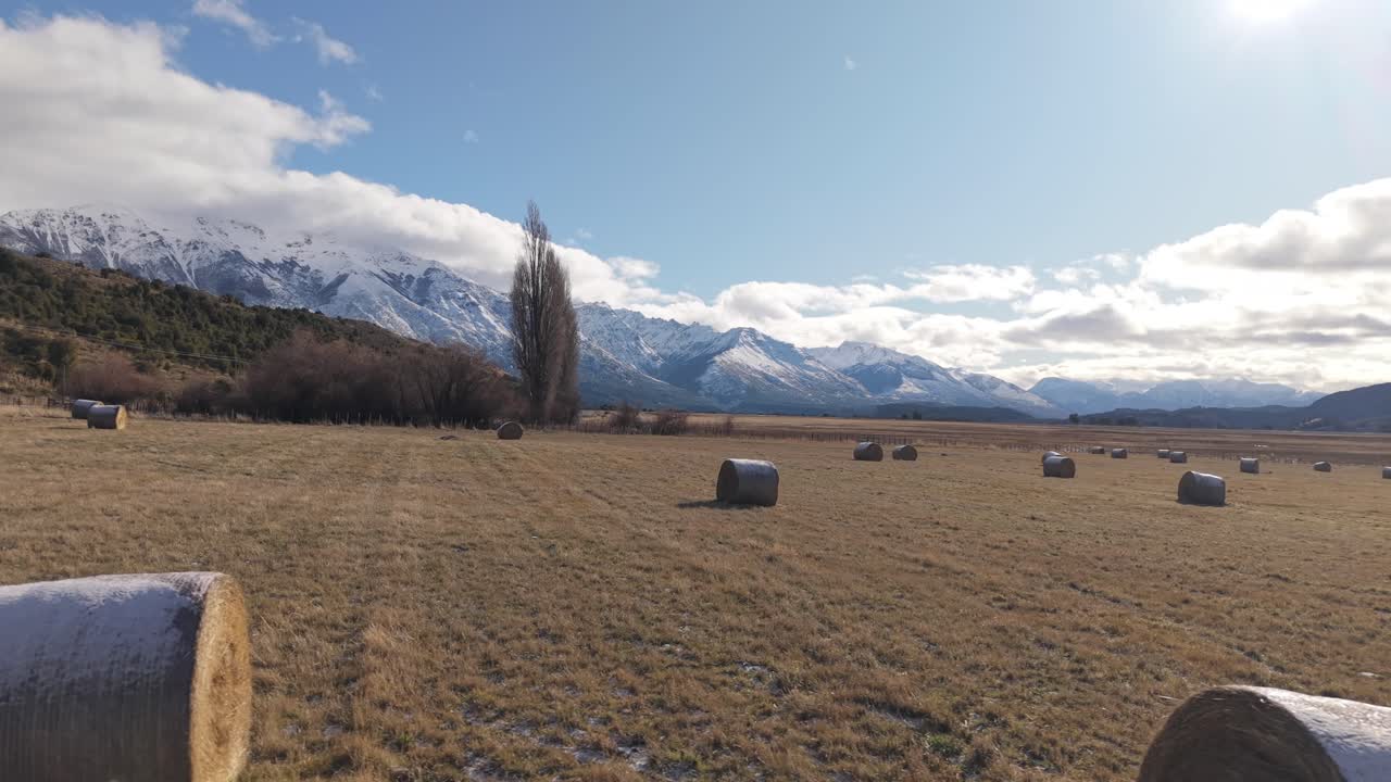 Hay bales scattered across field with Andes mountains in background, rural landscape and sustainable agriculture, Argentina