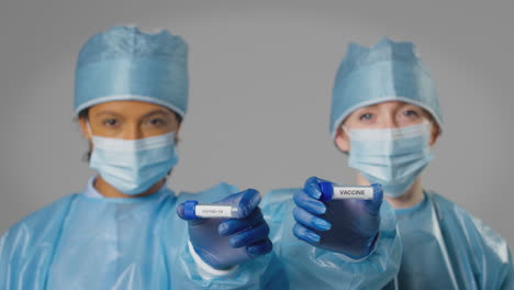 studio shot of female lab research workers in ppe holding test tubes labelled covid-19 and vaccine