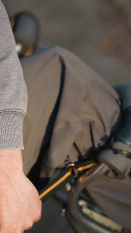 primer plano de la mano de la persona ajustando los binoculares en un entorno al aire libre borroso, con pantalones verde oliva y sudadera gris claro, centrarse en la acción de manipular los binoculares en un entorno natural