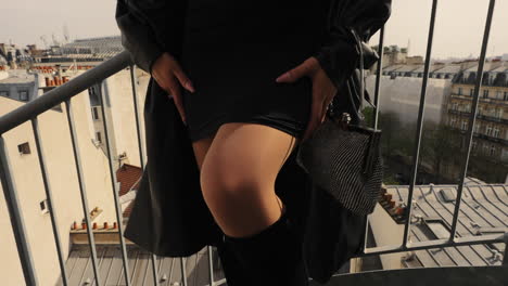 Close-up-of-a-beautiful-young-woman-legs,-wearing-a-black-dress,-standing-on-a-rooftop-in-Paris,-France