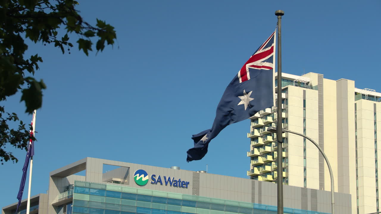 The SA Water building in Adelaide, Australia, with the Australian flag waving in the foreground. This video is perfect for projects related to Australia, business, water, or infrastructure.