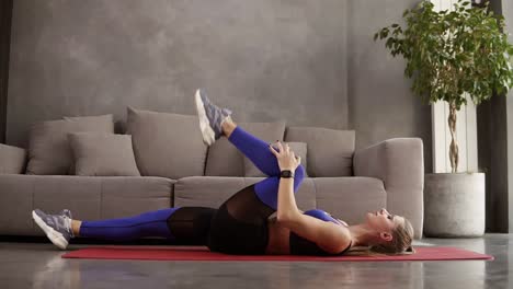 exercises for warming up. attractive sportive woman in sportwear is lying on the mat with the leg lifting to her torso. minimal interior room in loft design