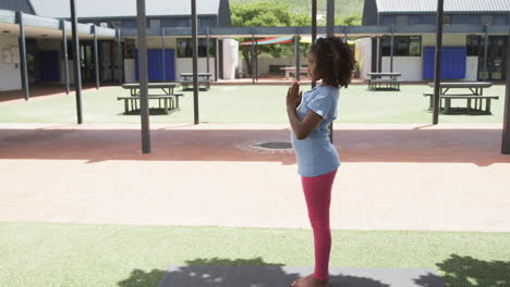 Biracial-girl-practices-yoga-in-a-sunny-schoolyard-with-copy-space