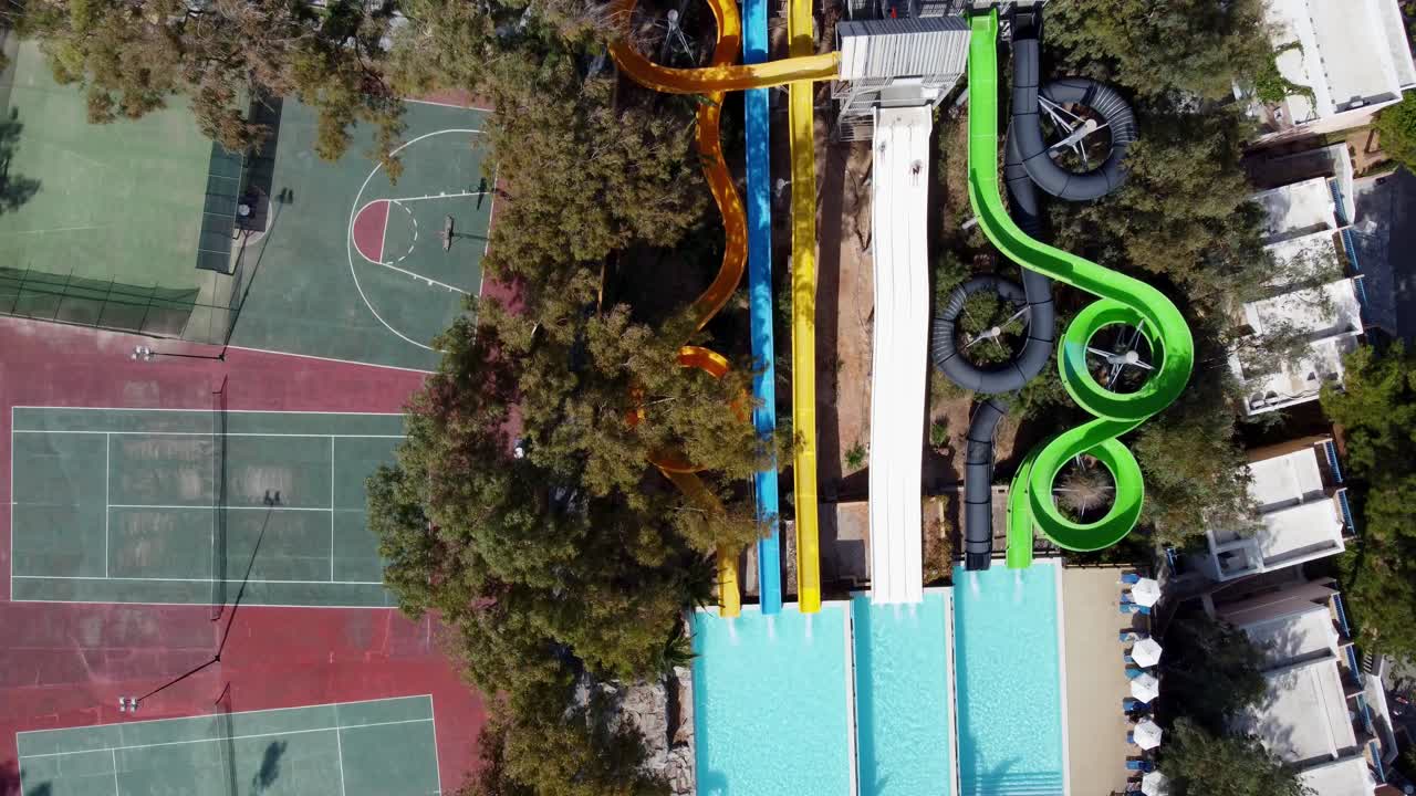 Drone hovers over water park with slides and tennis court - people slide down the slides
