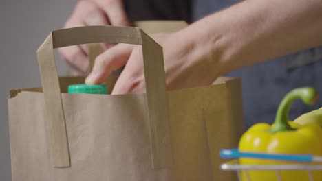 close up shot of person packing basic food items in supermarket shopping basket into paper bag