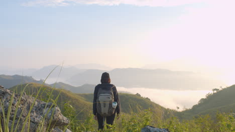 wide shot of young woman backpacker stopping to see the sunrise view on top of a mountain