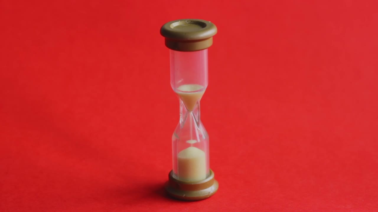 Time slipping away from a tiny sand timer on chroma red