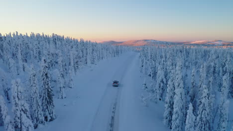 aerial view above vehicle travelling freezing snowy remote woodland road towards sunrise mountain landscape