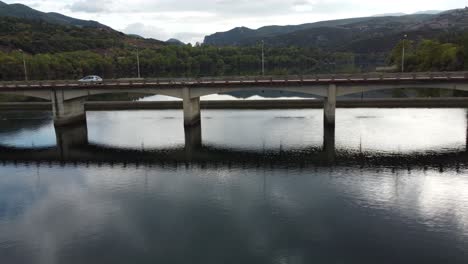 Dramatic-drone-shot-approaching-a-bridge-above-river-crystal-waters