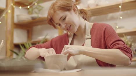 young woman sculpting earthenware vessel in pottery workshop