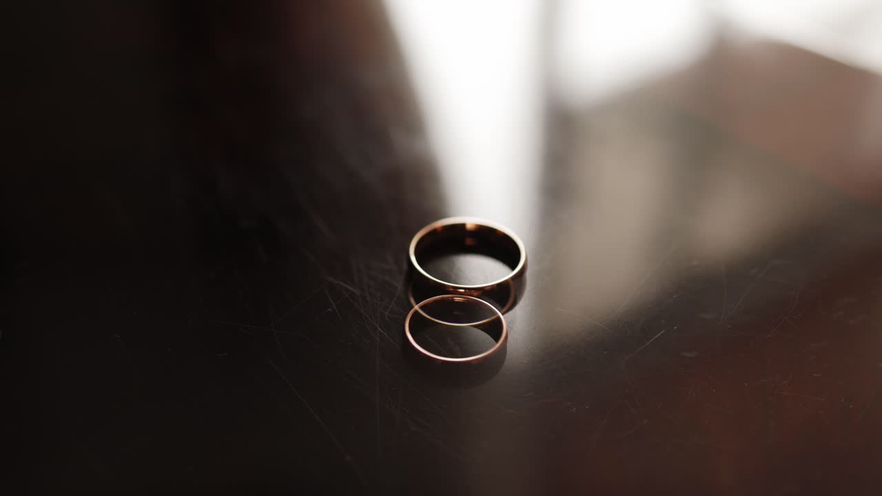 Close up of gold wedding bands on dark glossy surface with soft light