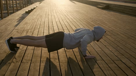 man doing push-ups on a wooden boardwalk at sunrise