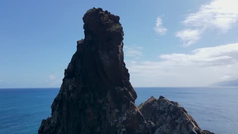 Aerial-drone-footage-captures-a-breathtaking-mountain-peak-overlooking-the-ocean,-with-birds-gracefully-soaring-through-the-expansive-blue-sky