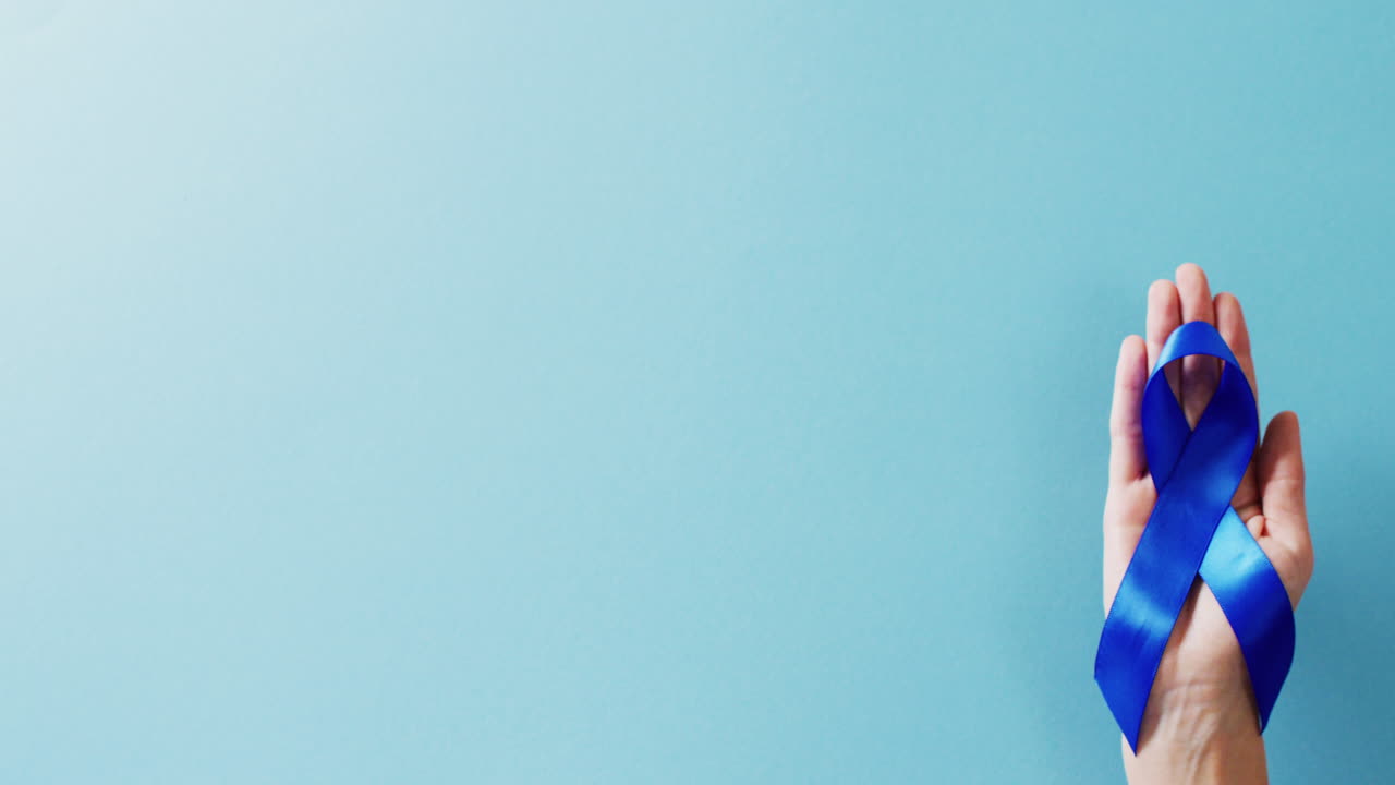 복사 공간이 있는 파란색 배경에 파란색 전립선 암 인식 리본을 들고 있는 손의 비디오