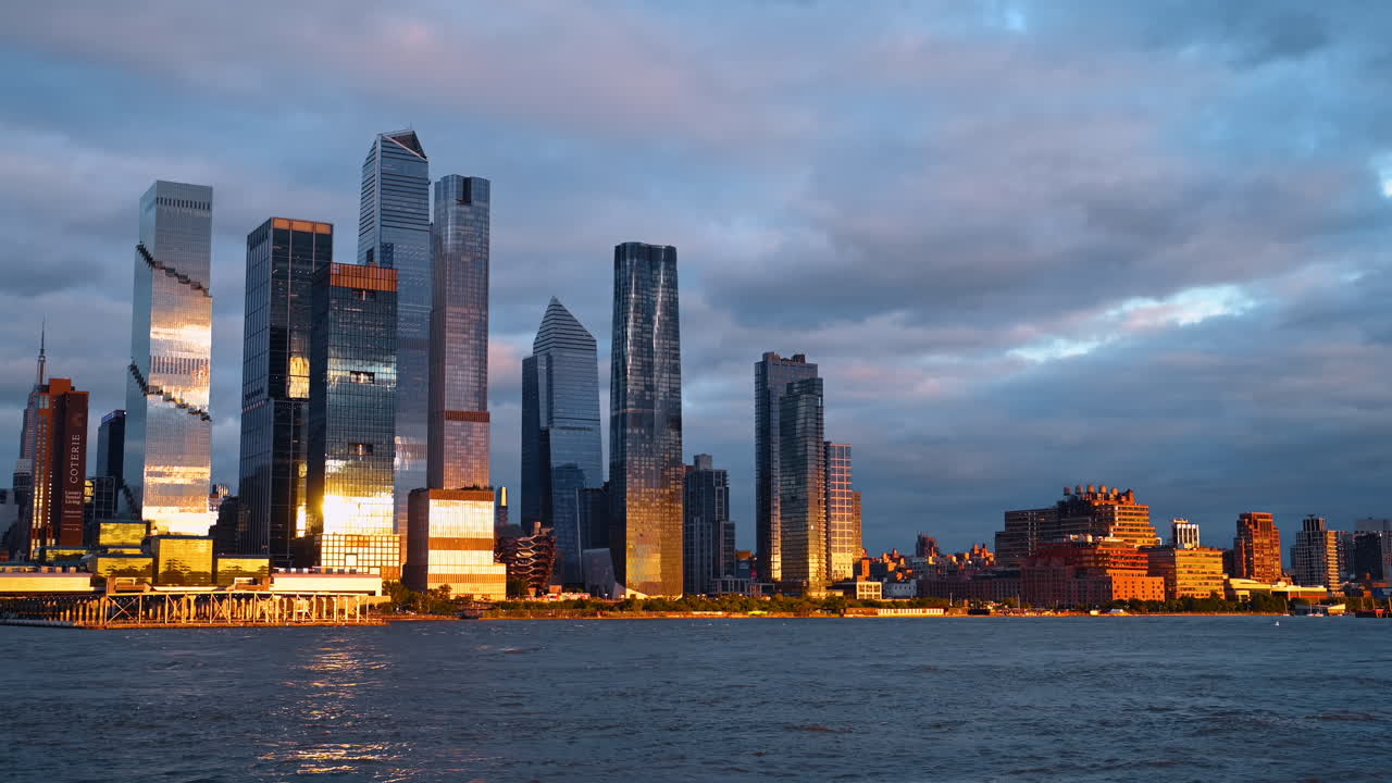 New York, USA, 5 October 2025: Hudson Yards skyline at golden hour across the river. Panoramic view of Manhattan skyscrapers glowing in the sunset light with river water in the foreground