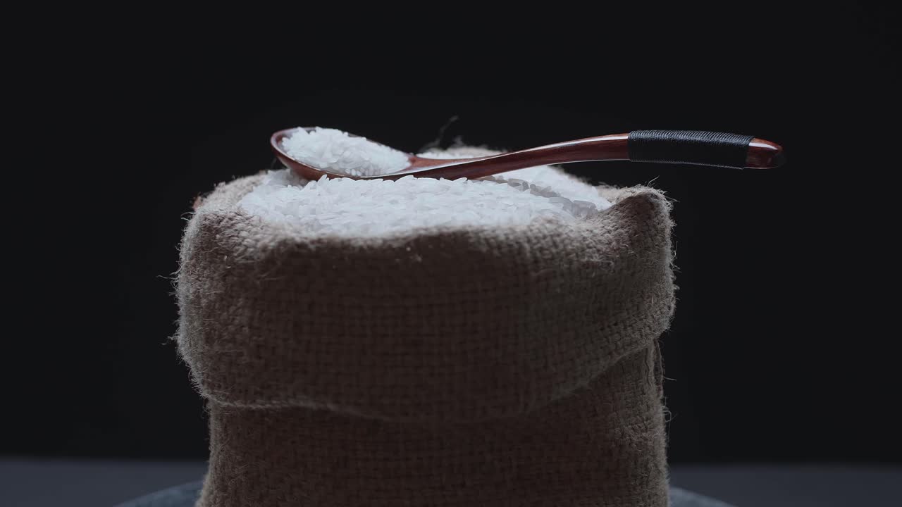 Rice Grains In The Wooden Spoon On A Rustic Bag  Rotating In Slow Motion