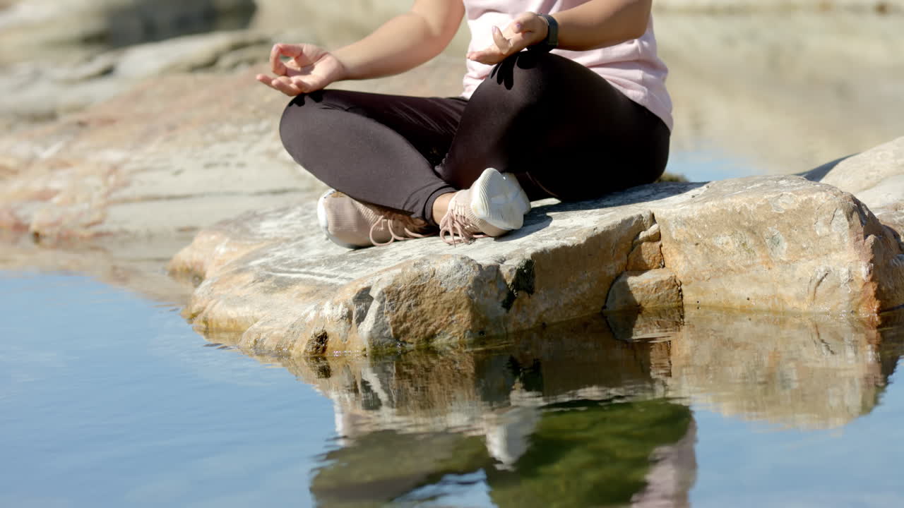 Meditating on rock by water, woman practicing mindfulness during mountain hike