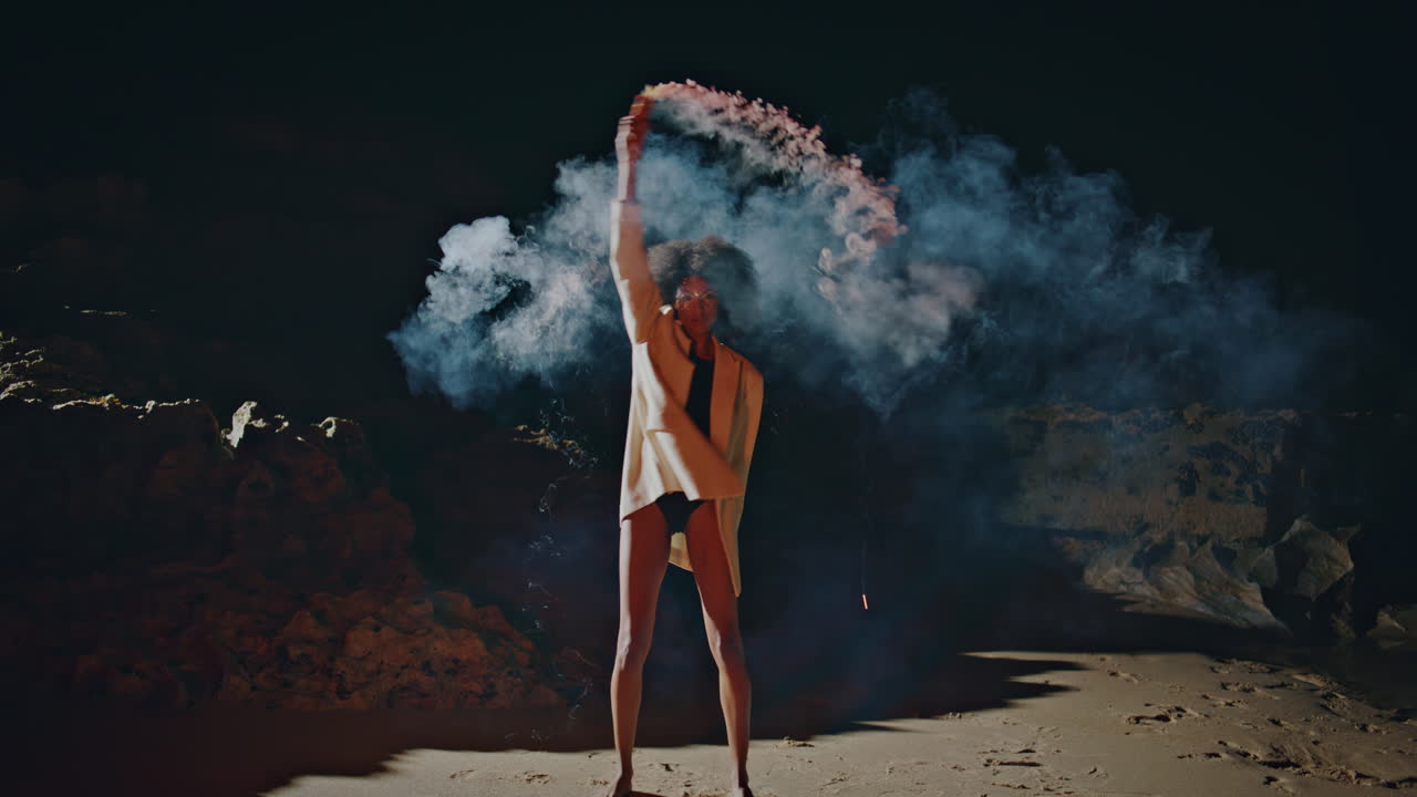 Woman waving smoke bomb at dark shore. Protest model holding grenade in light