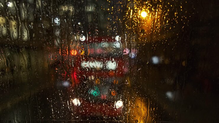 Rain falls down back window of London bus as buses and traffic pass behind out of focus