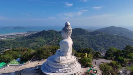 a serene aerial view of the big buddha statue in phuket, thailand, surrounded by lush hills and a clear blue sky