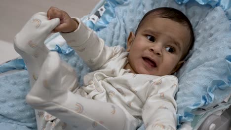 Baby-lying-on-a-blue-blanket-looking-puzzled,-daytime-indoor-shot