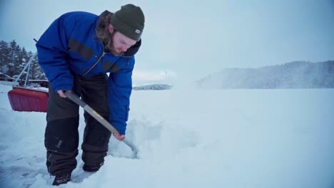 caucasian man in winter clothes shoveling thick snow