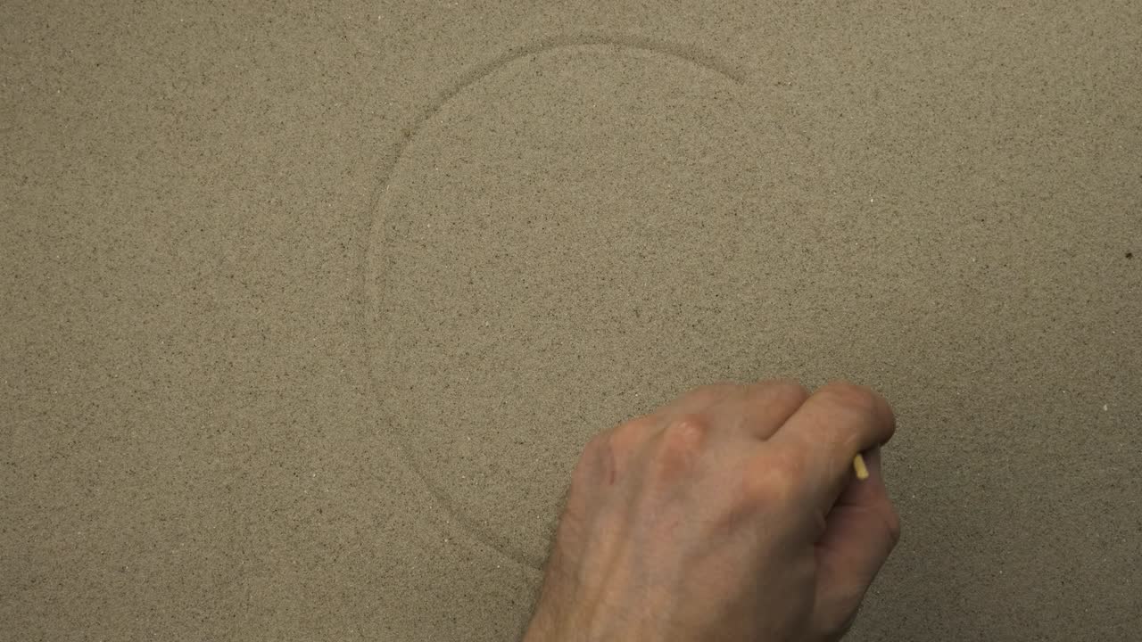 la mano masculina dibuja en la arena el rostro simbólico disgustado de una persona. vista superior.