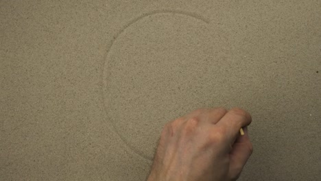 la mano masculina dibuja en la arena el rostro simbólico disgustado de una persona. vista superior.