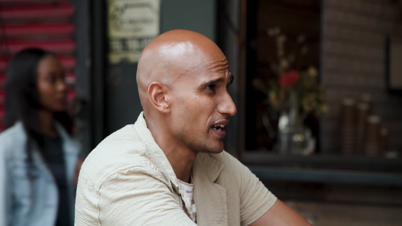 African American man sipping black-lidded coffee, sparking chat and gesturing by shop window
