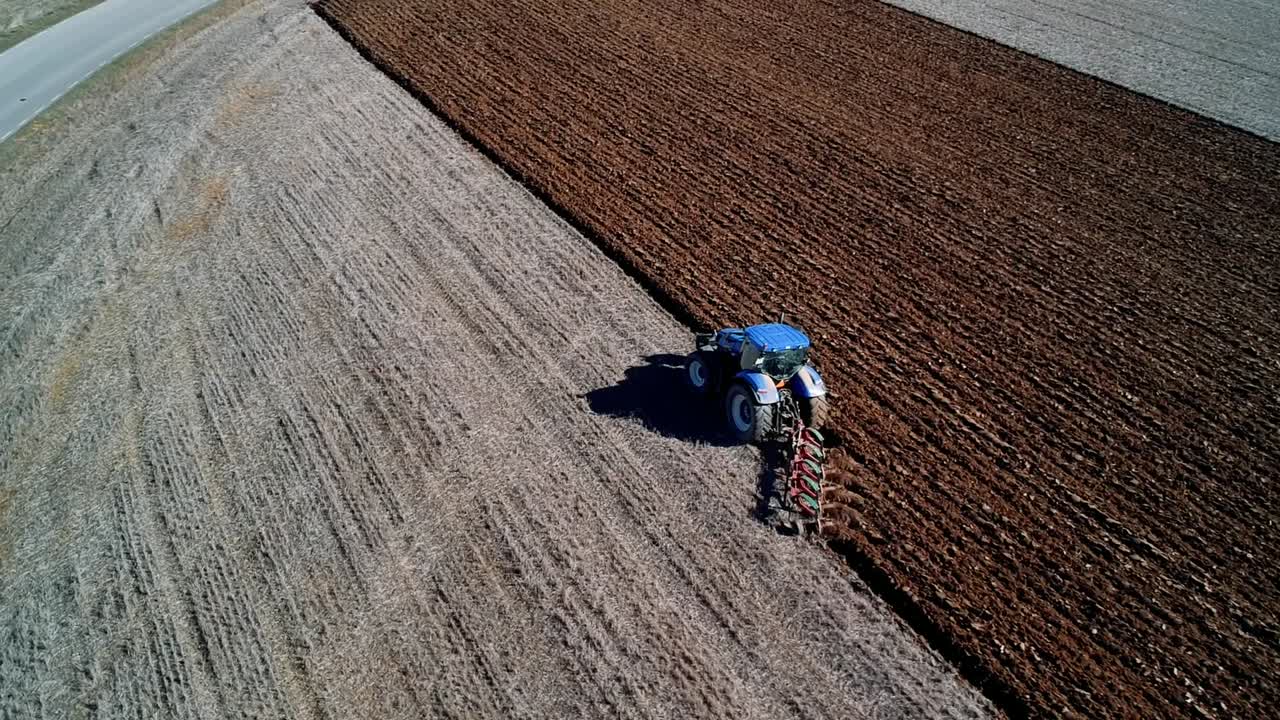 toma aérea enfocada en un tractor azul arando un campo cambiando el color del suelo