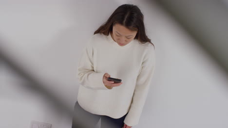 overhead shot of stressed or anxious woman leaning against wall at home reacting to internet or social media news message or story on mobile phone 1