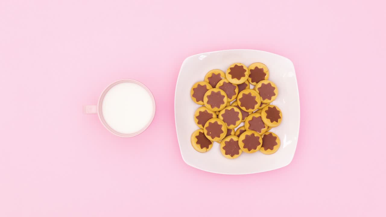 색 접시와 우유 한 잔의 초콜릿 쿠키는 분홍색 테마에서 원으로 움직입니다. 움직임을 멈추십시오.