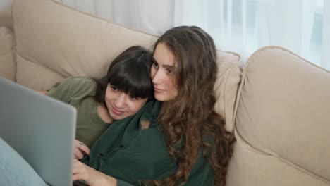 Two-girls-lay-on-the-couch-and-watching-movie-on-laptop-together