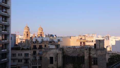 panoramic sunset view of our lady of the mount carmel church and city rooftops in gzira, malta on clear summer evening with high rise building in foreground