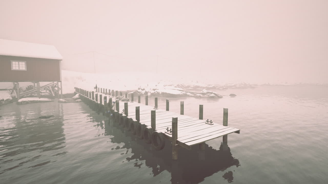 Snowy dock extends into foggy waters near a quiet cabin in winter