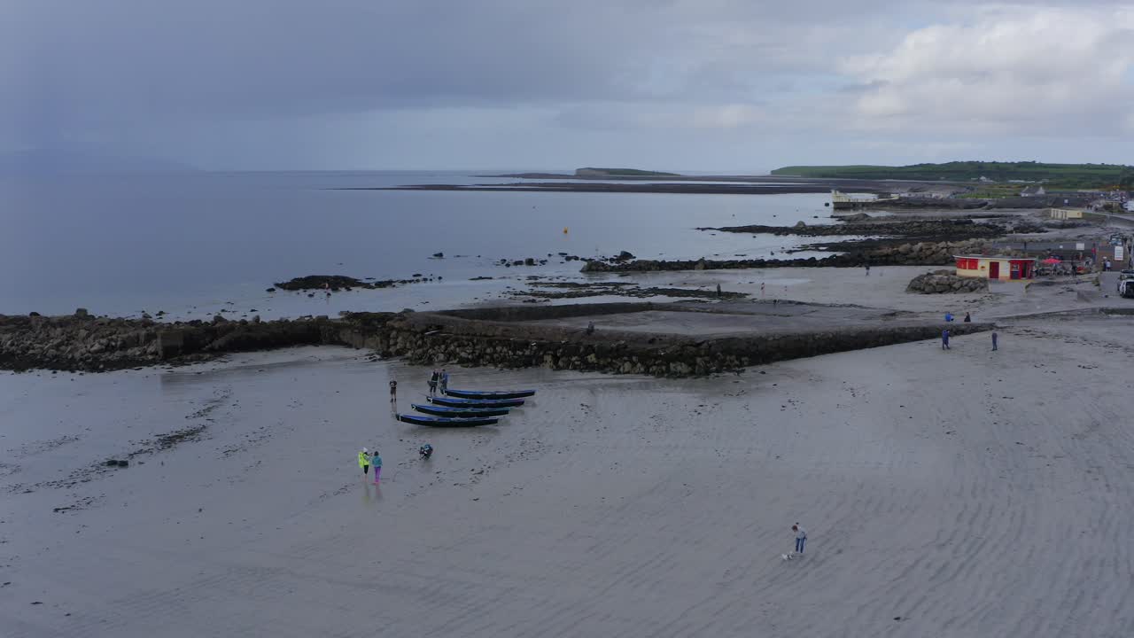Orbita del drone attorno a una barca currach su una spiaggia sabbiosa, con canoe all'alba cupa e un orizzonte bluastro